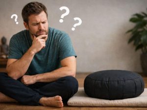 Man looking at a meditation cushion with question marks above his head, wondering if he needs a meditation cushion yet