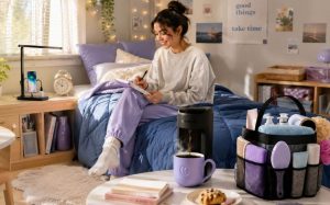 Cozy dorm room essentials setup featuring a young woman enjoying independent living in a warm, personalized dorm space with layered bedding, a bedside charging lamp, compact coffee maker, shower caddy organizer, and soft pastel decor for studying and relaxing.